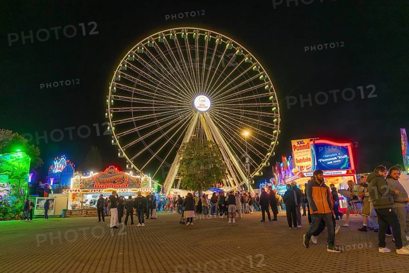 Large Ferris wheel lights up the night while people visit the stalls, Cannstatter Wasen folk festival, Stuttgart, Germany