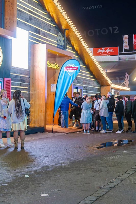 People standing in front of an illuminated marquee at night while waiting for admission, Cannstatter Wasen folk festival, Stuttgart, Germany