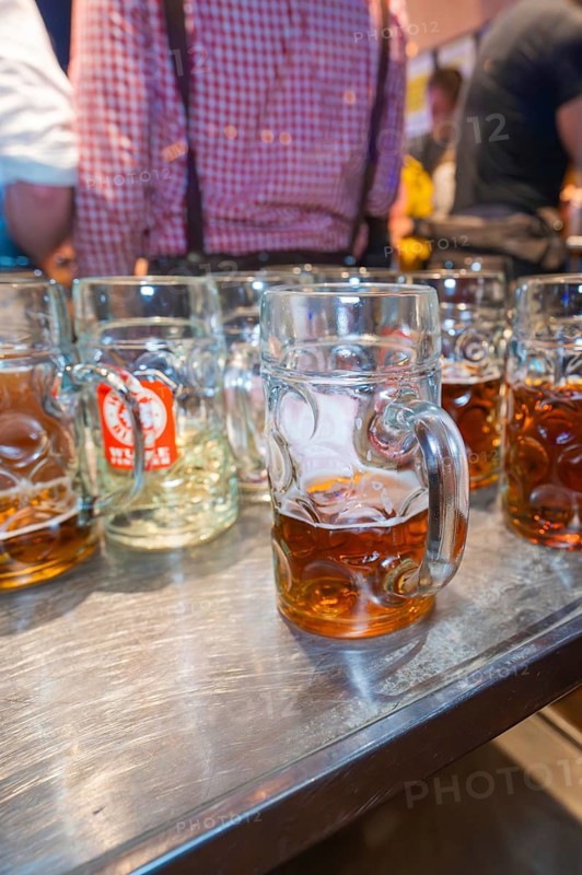 Large glass mugs of beer on a wooden table surface in a lively festival setting, Cannstatter Wasen folk festival, Stuttgart, Germany
