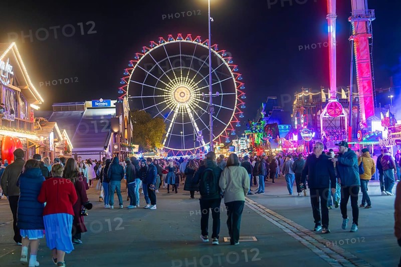 People walking on a festive square with a glowing Ferris wheel, Cannstatter Wasen folk festival, Stuttgart, Germany