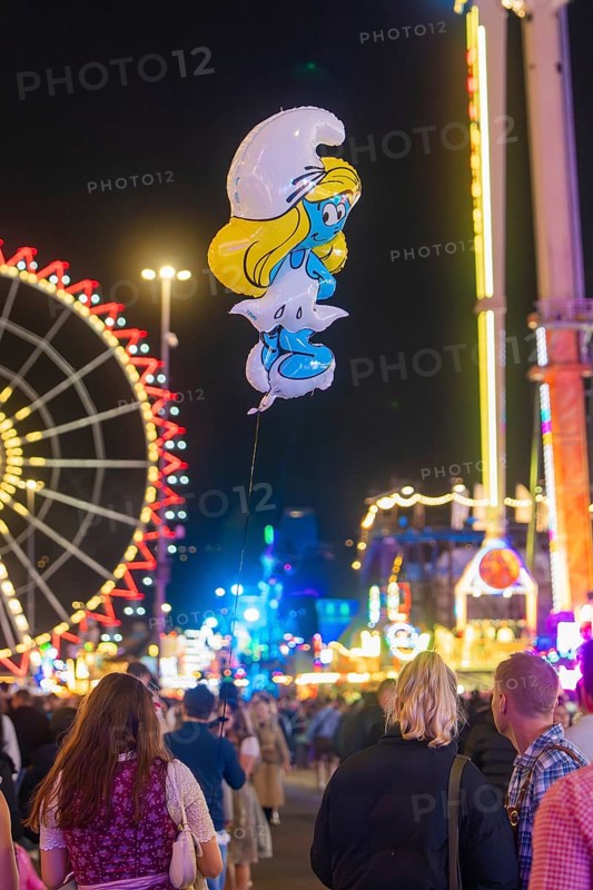 View of a Smurf balloon floating between a crowd at a funfair, with Ferris wheel in the background, Cannstatter Wasen funfair, Stuttgart, Germany