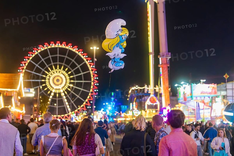 People enjoying the hustle and bustle of a fairground at night with a large Ferris wheel in the background, Cannstatter Wasen fairground, Stuttgart, Germany