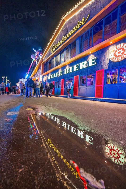 Reflection of the colourful lights of a beer hall on a wet street at night, Cannstatter Wasen folk festival, Stuttgart, Germany