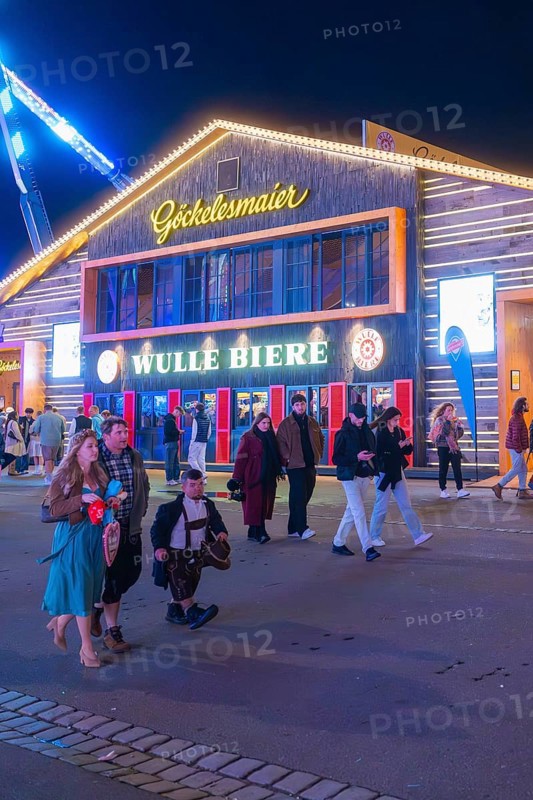 People strolling at night in front of an illuminated building at the funfair, Cannstatter Wasen folk festival, Stuttgart, Germany