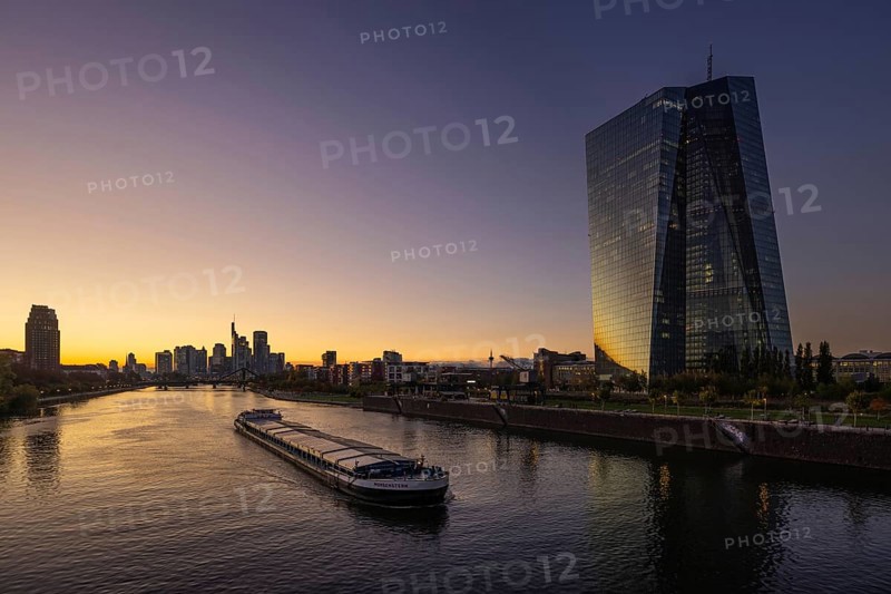 A boat cruises along the Main at sunset, in front of the European Central Bank (ECB) and the Frankfurt banking skyline, Frankfurt am Main, Hesse, Germany