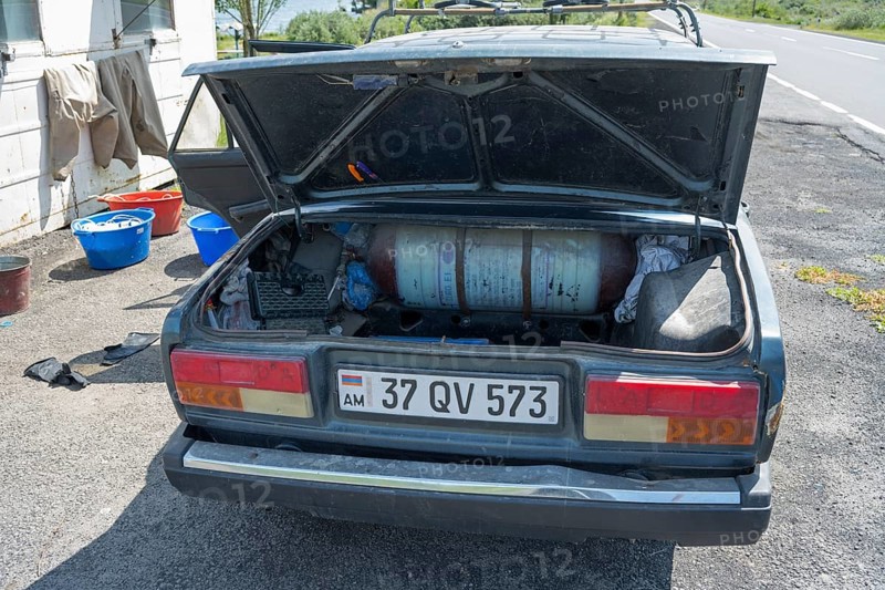 Old car with open boot, gas bottle and tools on a sunny day next to the road, car has gas tank retrofitted to be able to drive more cheaply, Armenia