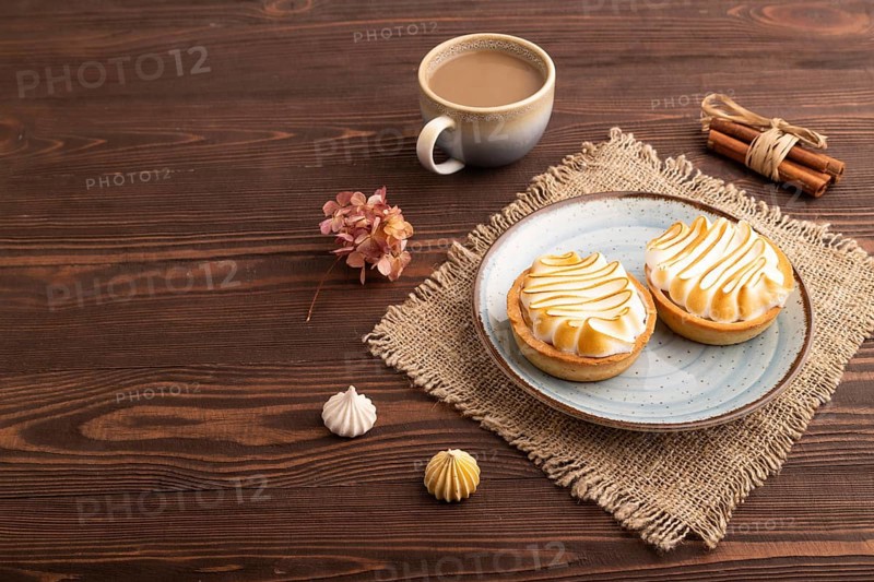 French lemon tart with meringue on brown wooden background, cup of coffee, linen textile, side view, copy space