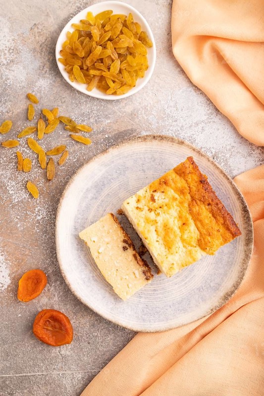 ?ottage cheese ?asserole, Curd cake, with dried apricots and raisins on brown concrete background and orange textile, top view, flat lay, close up, minimalism