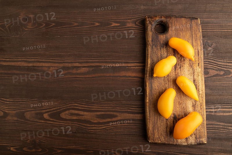 Yellow tomatoes on cutting board on brown wooden background. Top view, copy space, flat lay. healthy food, vegetable, minimalism