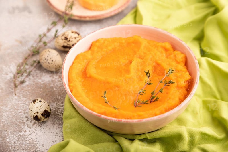 Sweet potato porridge in ceramic bowl on brown concrete background and green textile. Diet, healthy eating concept. side view, close up, selective focus