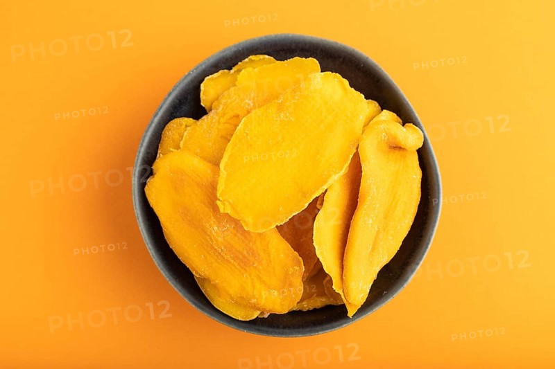 Dried Mango in blue ceramic bowl on orange pastel paper background. Top view, copy space, flat lay. healthy food, minimalism