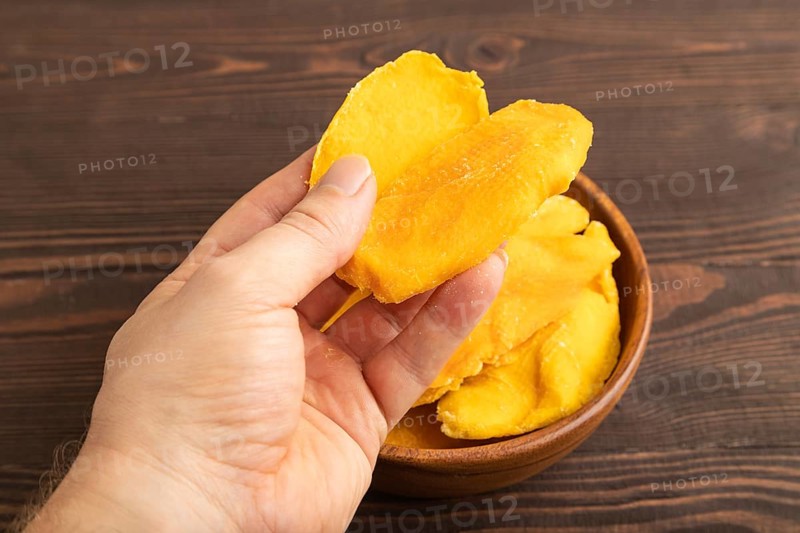 Dried Mango in wooden bowl with hand on brown wooden background. Side view, close up. healthy food, minimalism