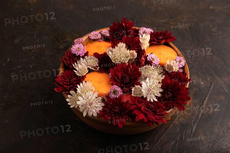 Wooden bowl with carrot slices and red Chrysanthemum flowers, Astrantia flowers, flower salad on black concrete background, side view, close up, minimalism