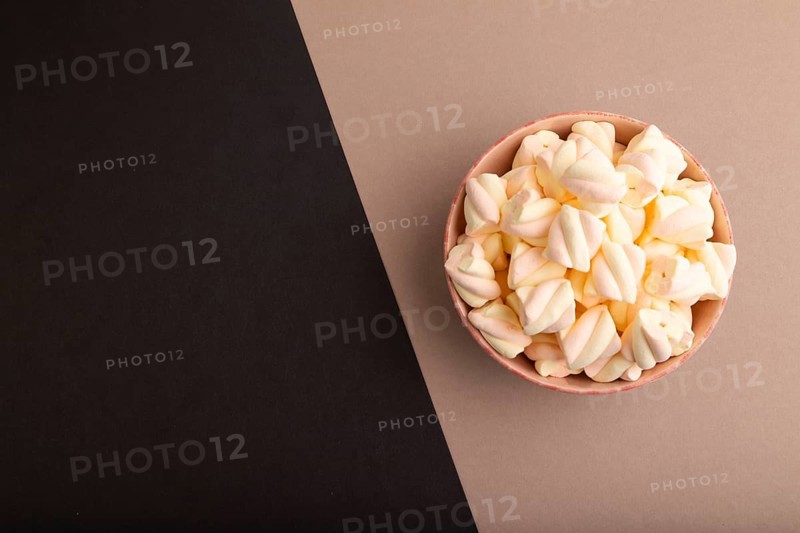 Orange and pink marshmallow in ceramic bowl on black and beige pastel paper background, top view, flat lay, copy space, minimalism