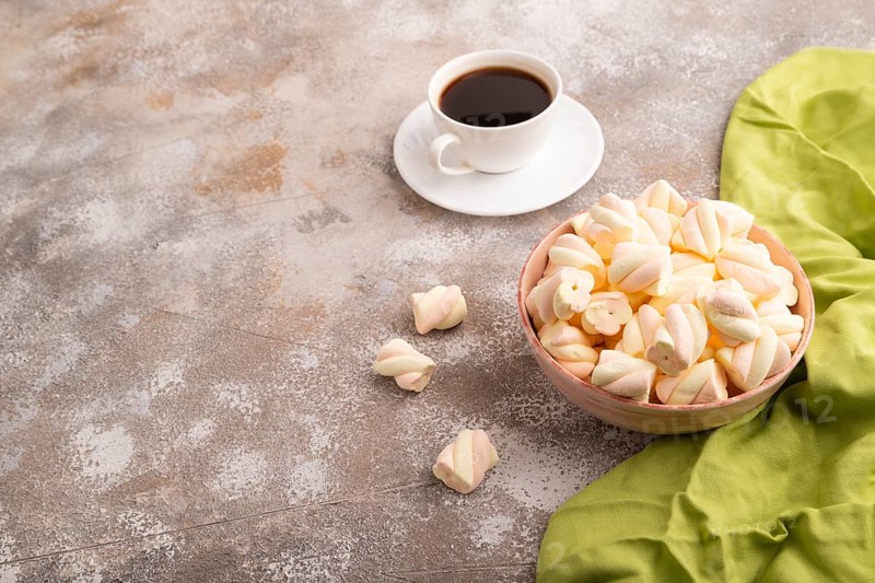Orange and pink marshmallow in ceramic bowl on brown concrete background and green textile, side view, copy space, minimalism