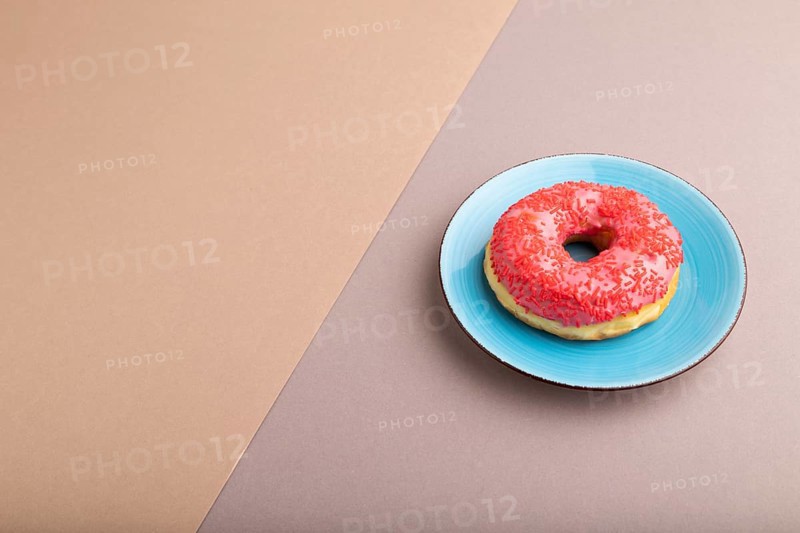 Pink Donut with sprinkles on blue ceramic plate on beige and gray pastel paper background, side view, copy space, minimalism