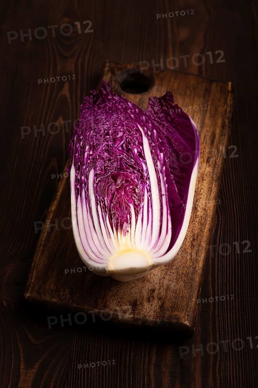 Purple Chinese cabbage on cutting board on brown wooden background, side view, close up, minimalism