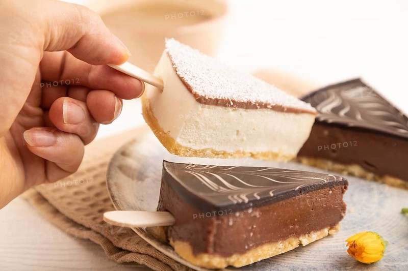 Chocolate and Vanilla Cake pops Marshmallow with hand with cup of coffee on white wooden background and beige linen textile. side view, close up, selective focus hold