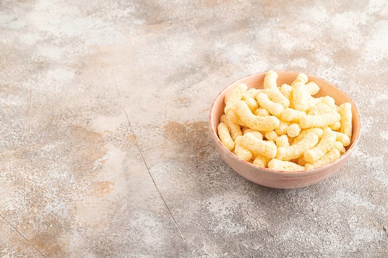 Corn flakes sticks with caramel in ceramic bowl on gray concrete background. Side view, copy space