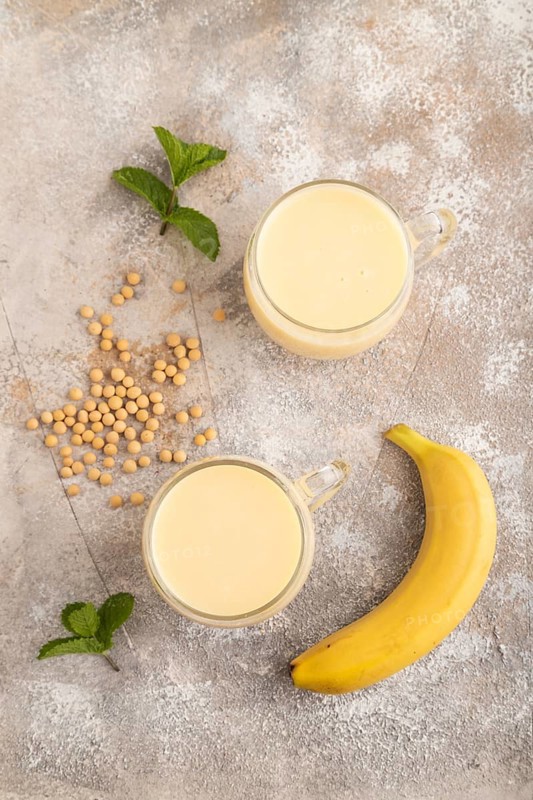 Organic non dairy banana and soy milk in glass on brown concrete background. Vegan healthy food concept, flat lay, top view, close up