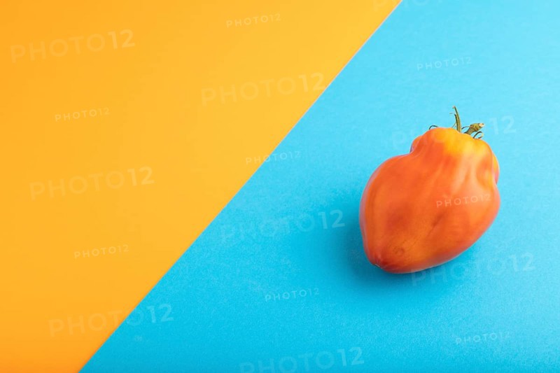 Red Heart Shape tomato on blue and orange pastel paper background. Side view, copy space. healthy food, vegetable, minimalism