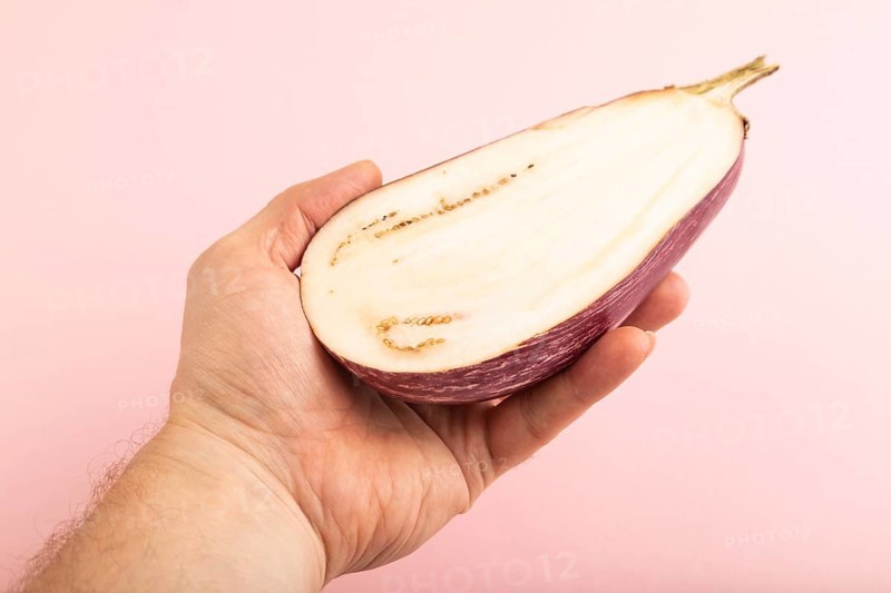 Hand holding sliced Purple eggplant with white stripes on pink pastel background. Side view, copy space. Tropical, healthy food, vegetable, minimalism