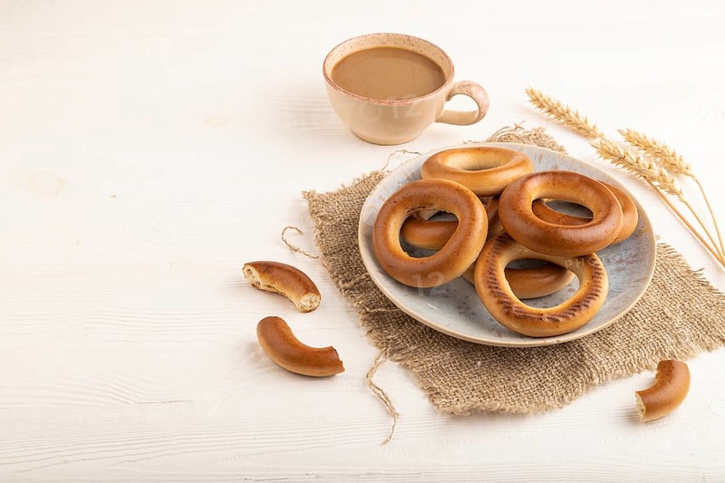 Homemade Ring Bagel with cup of coffee on white wooden background and linen textile. side view, copy space
