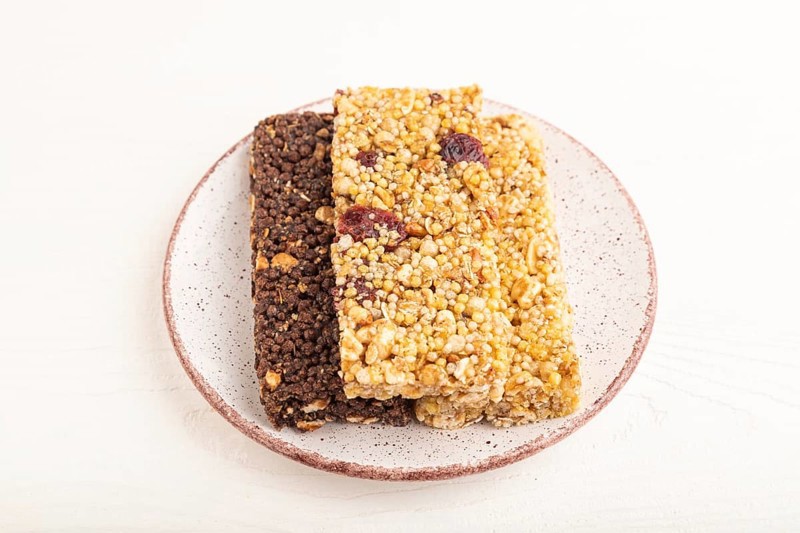 Granola bars with caramel, nuts, flakes in ceramic plate on white wooden background. Side view, close up