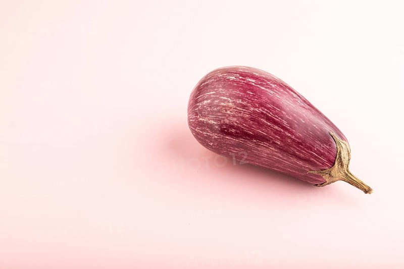 Purple eggplant with white stripes on pink pastel background. Side view, copy space. Tropical, healthy food, vegetable, minimalism