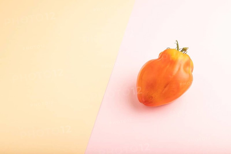 Red Heart Shape tomato on pink and orange pastel paper background. Side view, copy space. healthy food, vegetable, minimalism