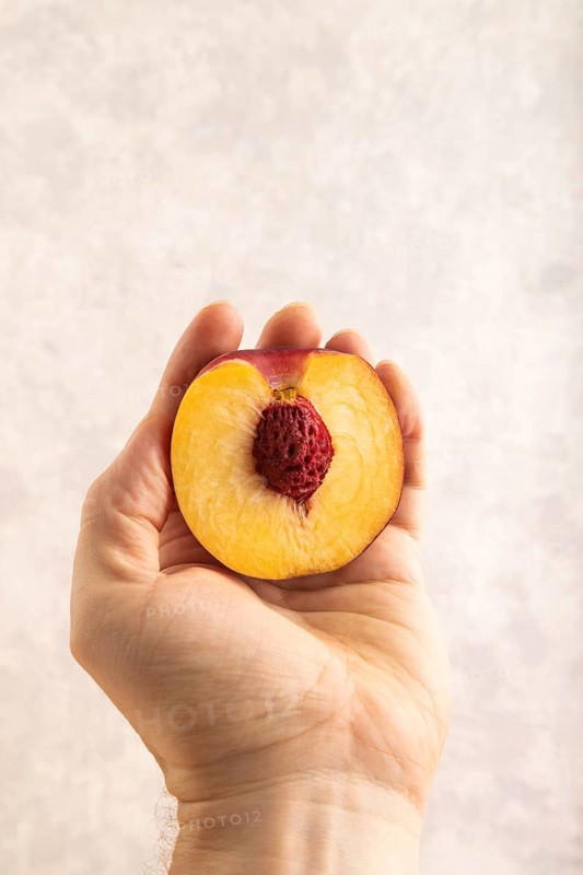 Peach Cut in half with hand on brown concrete background. Side view, copy space. healthy food, vegetable, minimalism