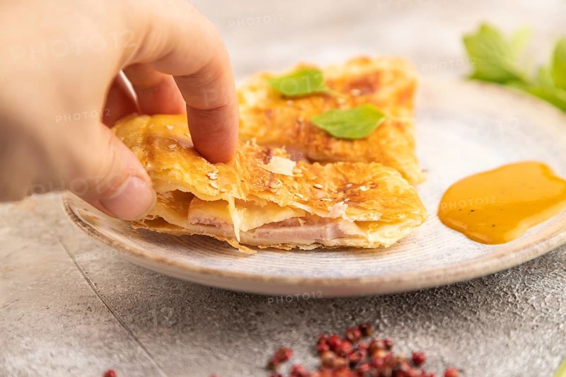 Fried homemade Khachapuri cake with hand with cheese and meat, fried in pan. Traditional Georgian cuisine on brown concrete background. Side view, close up, selective focus