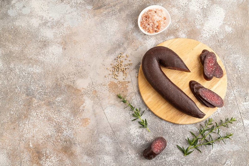 Sujuk sausage on wooden cutting board with pepper and herbs on brown concrete background. Top view, flat lay, copy space