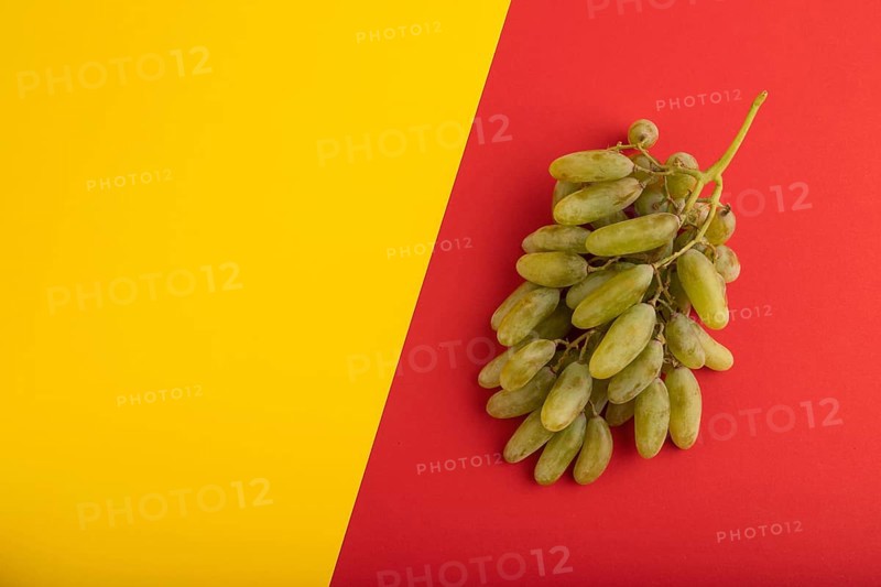 Green grapes on yellow and red paper pastel background. Top view, flat lay, copy space. healthy food, minimalism