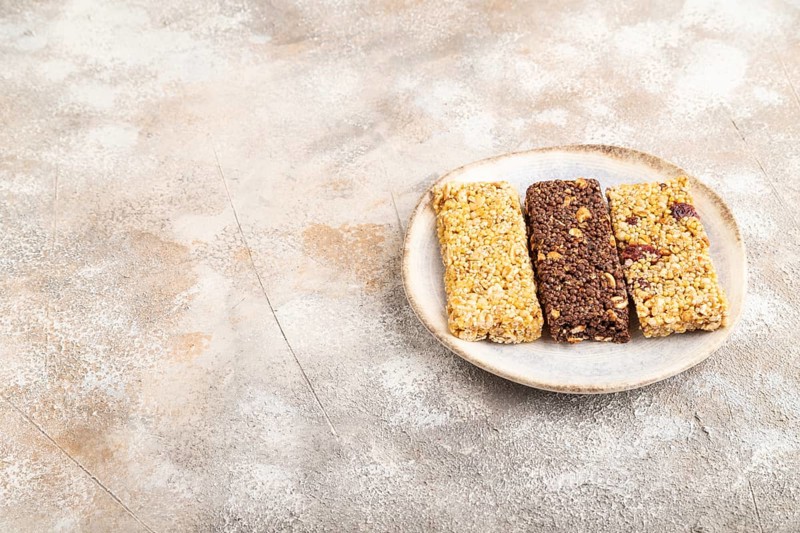 Granola bars with caramel, nuts, flakes in ceramic plate on brown concrete background. Side view, copy space