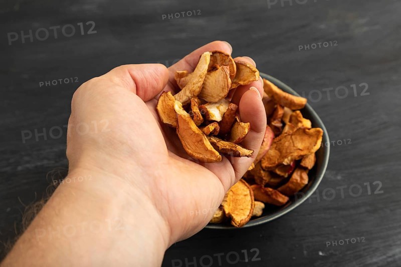 Dried Apples in ceramic bowl with hand on black wooden background. Side view, close up. healthy food, minimalism. sweet hold