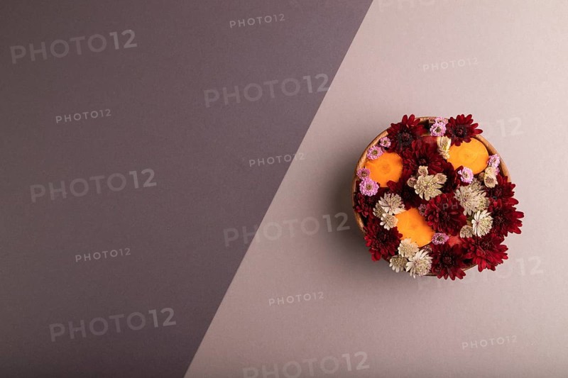 Wooden bowl with carrot slices and red Chrysanthemum flowers, Astrantia flowers, flower salad on beige and gray pastel paper background, top view, flat lay, copy space, minimalism