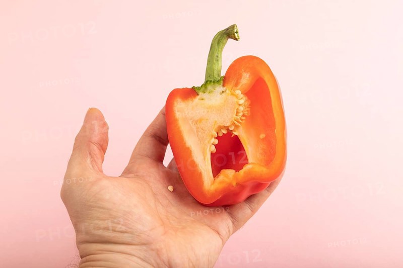 Hand holding sliced Red Cutted pepper on pink pastel background. Side view, copy space. Tropical, healthy food, vegetable, minimalism