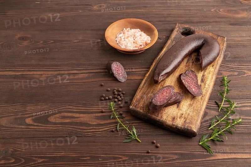 Sujuk sausage on wooden cutting board with pepper and herbs on brown wooden background. Side view, copy space