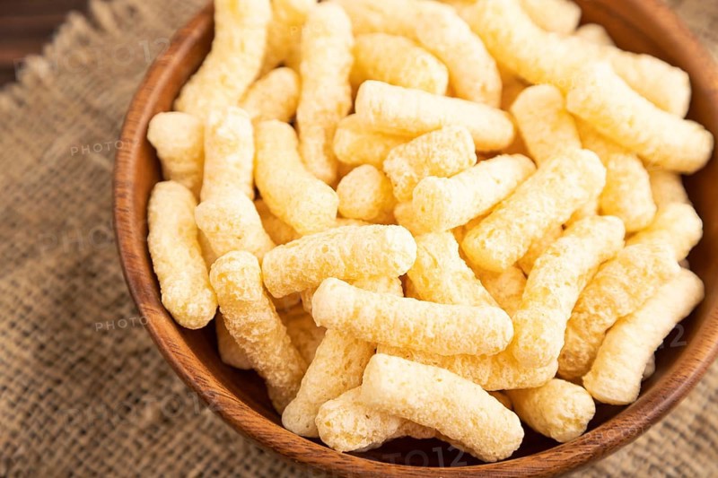 Corn flakes sticks with caramel in wooden bowl on brown wooden background and linen textile. Side view, close up, selective focus