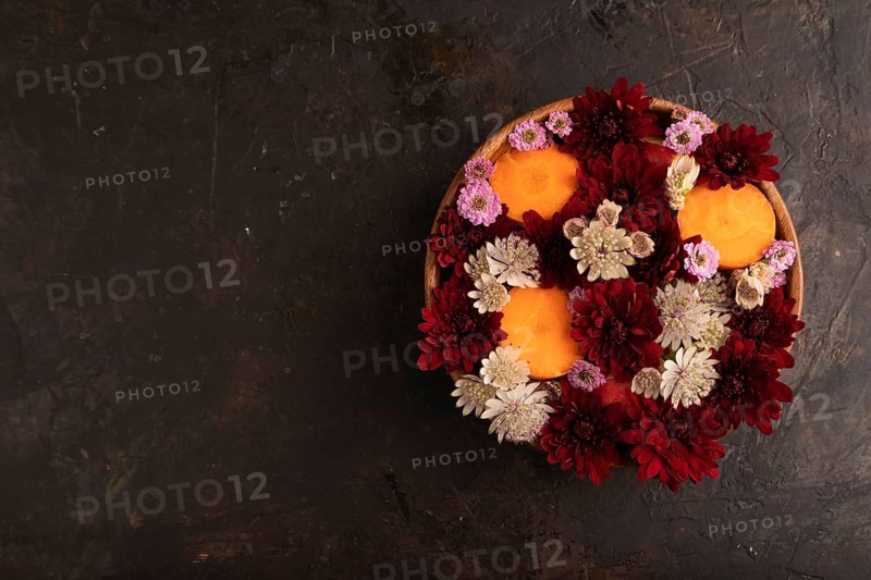 Wooden bowl with carrot slices and red Chrysanthemum flowers, Astrantia flowers, flower salad on black concrete background, top view, flat lay, copy space, minimalism
