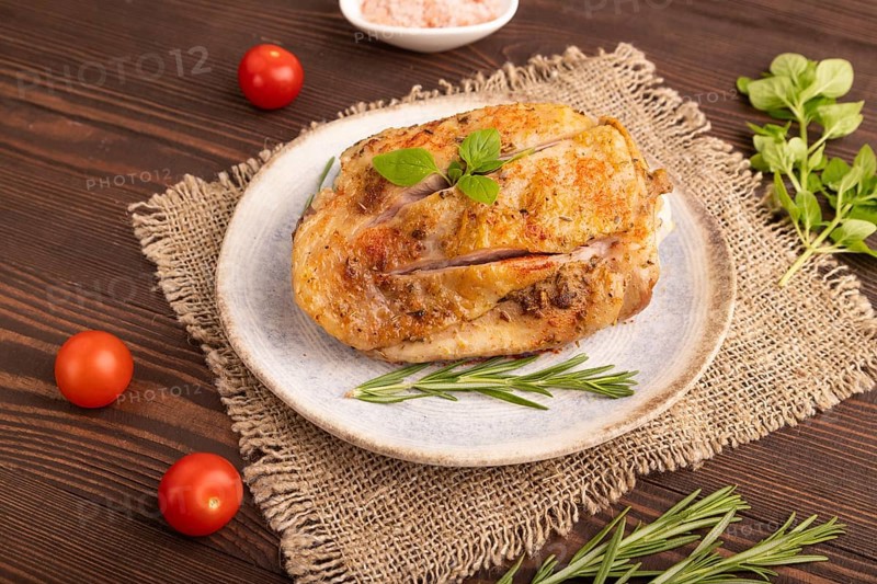 Fried Turkey Thigh with spices and rosemary on plate on brown wooden background and linen textile. side view, close up