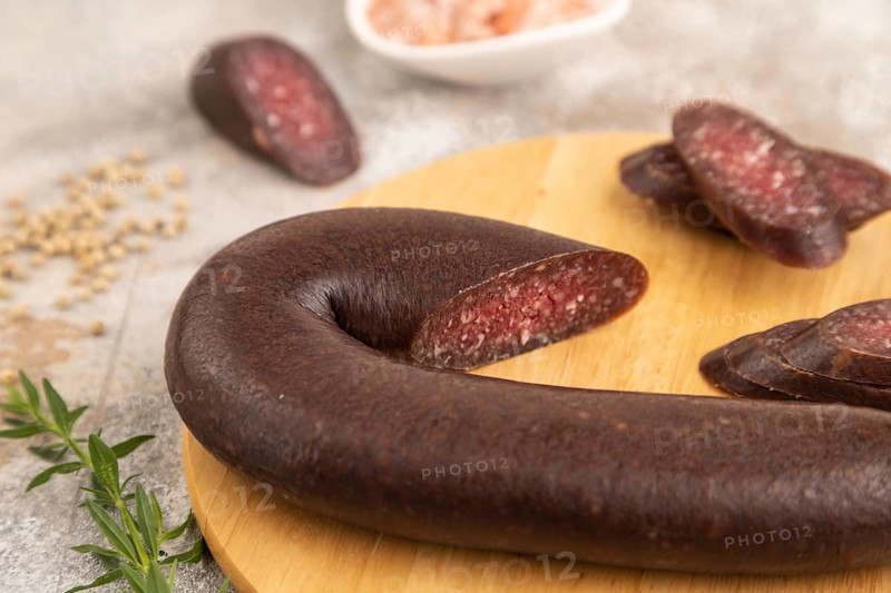 Sujuk sausage on wooden cutting board with pepper and herbs on brown concrete background. Side view, close up, selective focus
