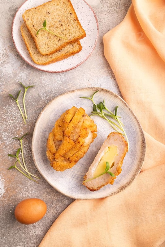 Chicken Schnitzel on blue plate with microgreen on brown concrete background and orange linen textile. top view, flat lay, close up