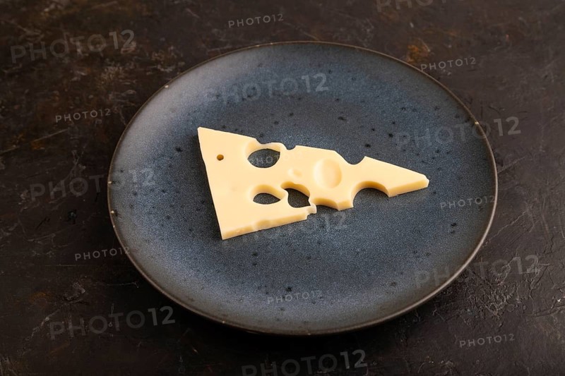Piece of cheese with holes on blue plate on black concrete background, side view, close up, minimalism
