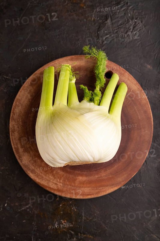 Fresh Fennel bulb on wooden cutting board on black concrete background, top view, flat lay, copy space, minimalism