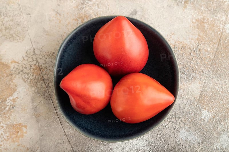 Red Heart shape tomatoes in blue bowl on brown concrete background. Top view, copy space, flat lay. healthy food, vegetable, minimalism