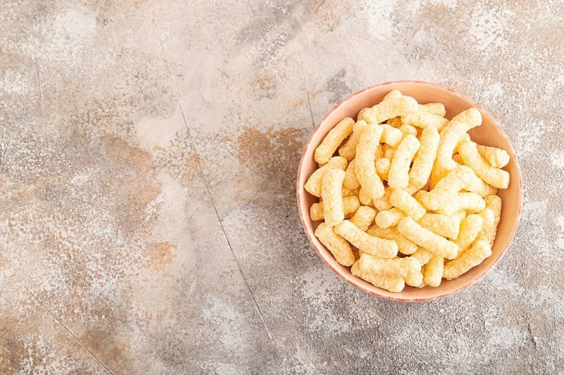 Corn flakes sticks with caramel in ceramic bowl on gray concrete background. Top view, flat lay, copy space