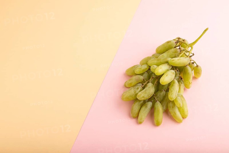 Green grapes on orange and pink paper pastel background. Side view, copy space. healthy food, minimalism
