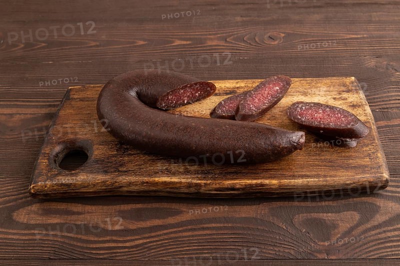 Sujuk sausage on wooden cutting board with pepper and herbs on brown wooden background. Side view, close up